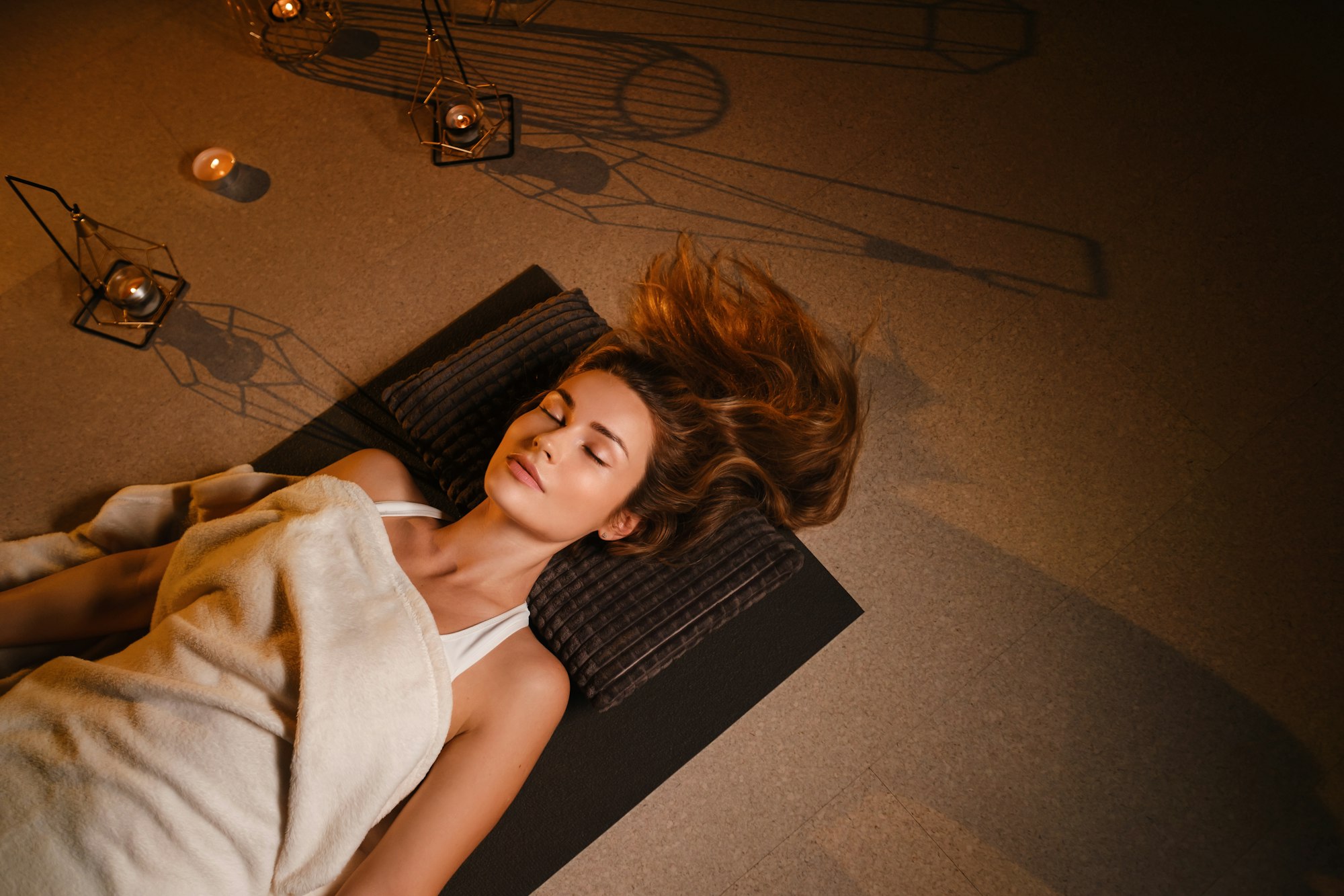 A woman lies on the floor covered with a blanket with her eyes closed and relaxes after a workout