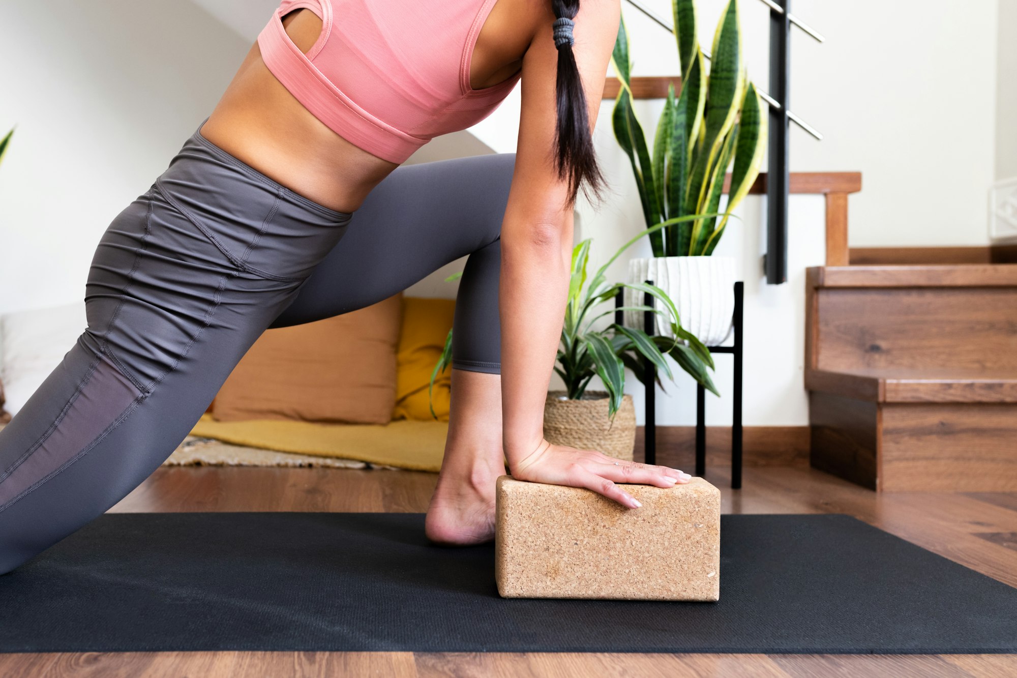 Unrecognizable woman doing yoga twist at home with help of cork yoga block.